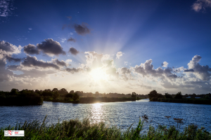 Zonnestralen vanachter de wolken vandaan over het water in Schipsloot Roderwolde Drenthe