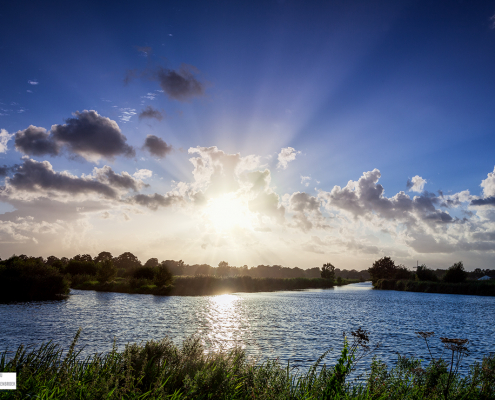 Zonnestralen vanachter de wolken vandaan over het water in Schipsloot Roderwolde Drenthe