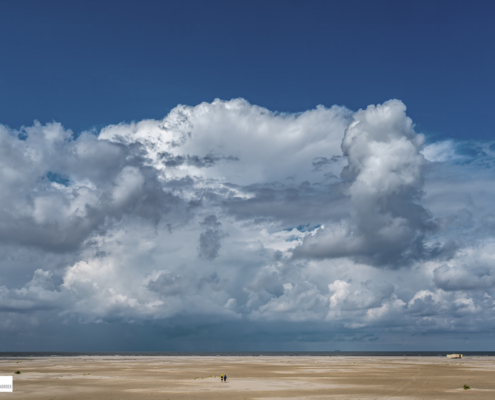 Enorme wolkenlucht en 2 mensen op een verlaten strand